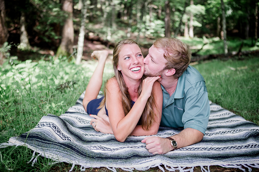 Kissing her cheeks laying on their stomachs engagement photo by Knoxville Wedding Photographer, Amanda May Photos.