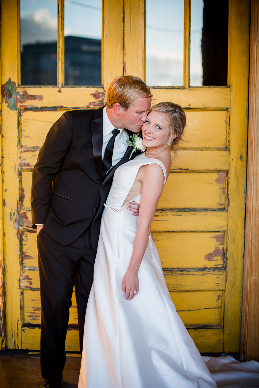 Kissing cheek in front of yellow door at this wedding at The Standard by Knoxville Wedding Photographer, Amanda May Photos.