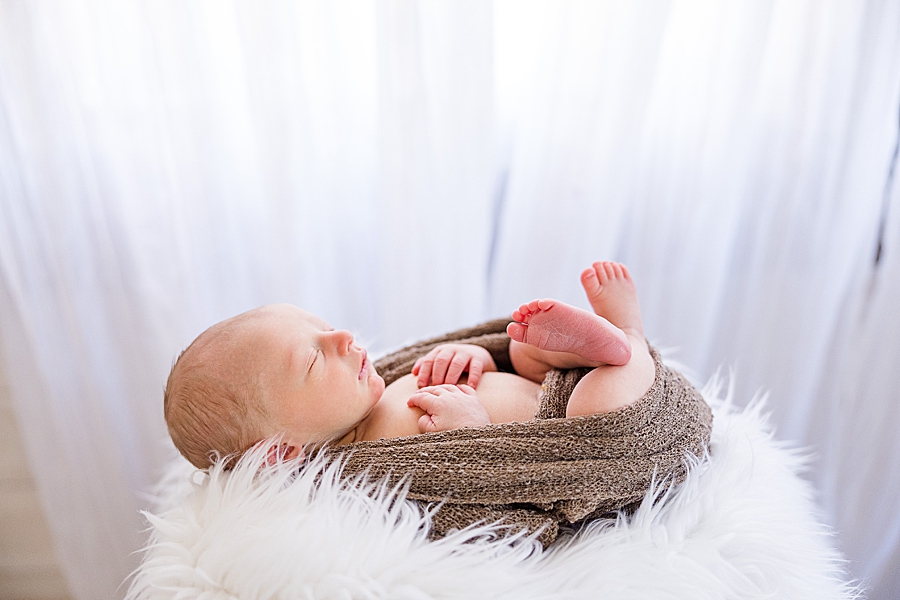 newborn curled up in a brown swaddle