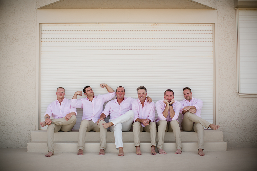 Grooms with groomsmen sitting and joking around in front of wall at this Daytona Beach Wedding by Destination Wedding Photographer, Amanda May Photos.