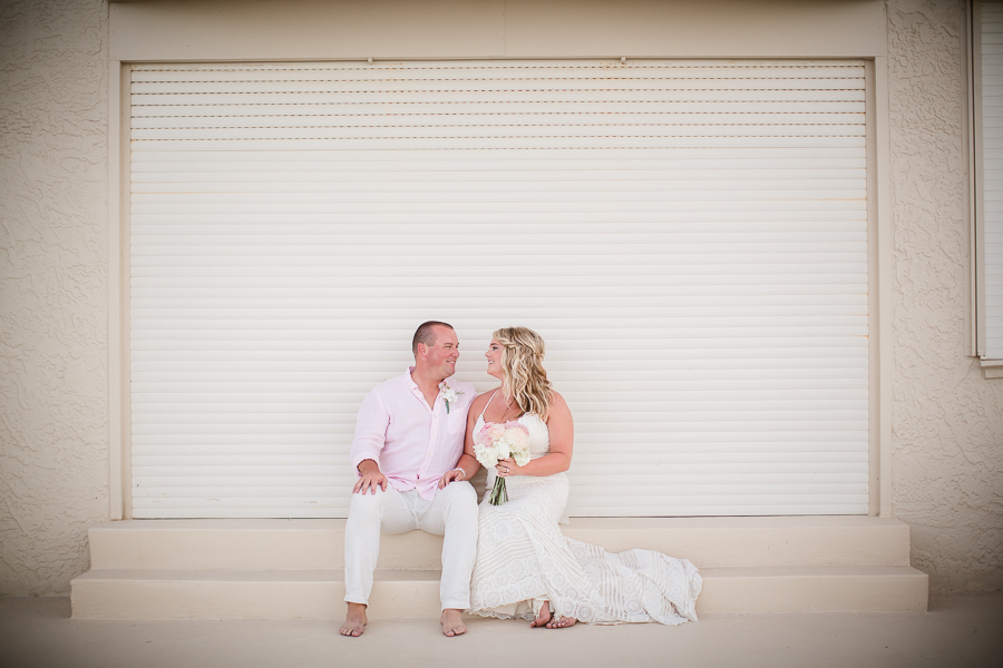 Bride and groom sitting in front of wall looking at each other at this Daytona Beach Wedding by Destination Wedding Photographer, Amanda May Photos.