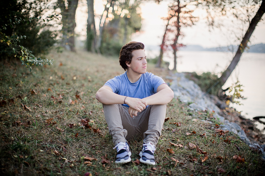 Sitting with elbows around his knees with the sunset behind him at this Maryville, TN Senior session by Knoxville Wedding Photographer, Amanda May Photos.