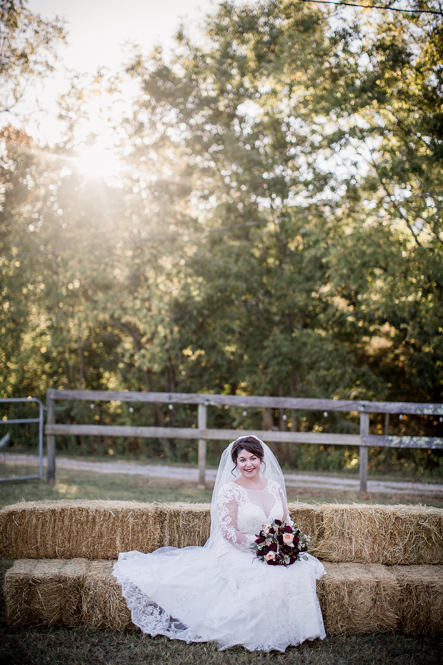 Sitting on hay bales with sun flare at this bridal session at The Barn at High Point Farms by Knoxville Wedding Photographer, Amanda May Photos.
