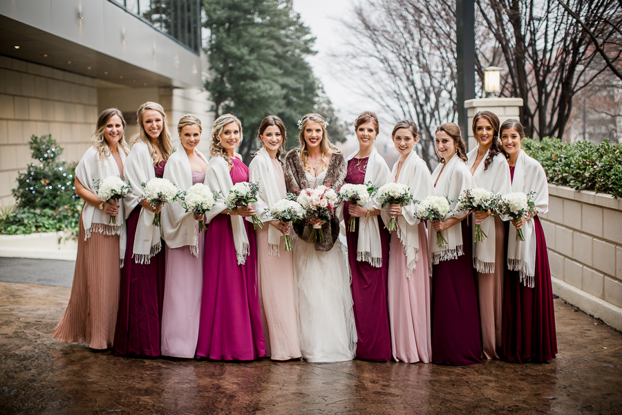 Angled in toward the bride smiling at the camera during the bride and bridesmaids pictures at this winter wedding at Knoxville Wedding Venue, Jackson Terminal, by Knoxville Wedding Photographer, Amanda May Photos.