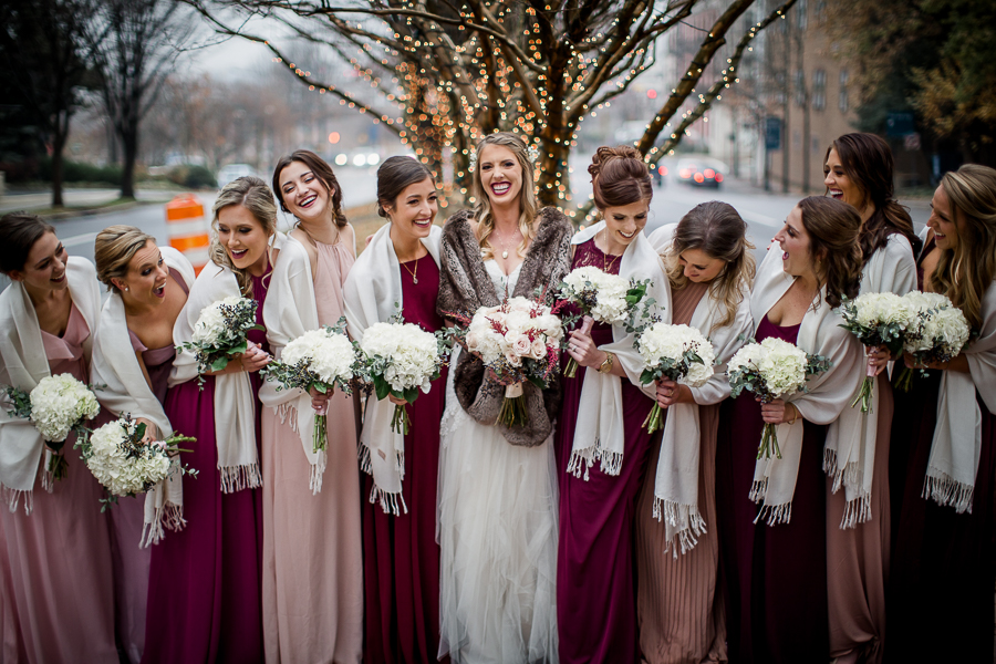 Standing in front of christmas lights on the tree during the bride and bridesmaids pictures at this winter wedding at Knoxville Wedding Venue, Jackson Terminal, by Knoxville Wedding Photographer, Amanda May Photos.