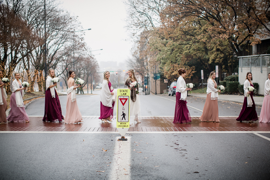 Crossing the street in single file during the bride and bridesmaids pictures at this winter wedding at Knoxville Wedding Venue, Jackson Terminal, by Knoxville Wedding Photographer, Amanda May Photos.