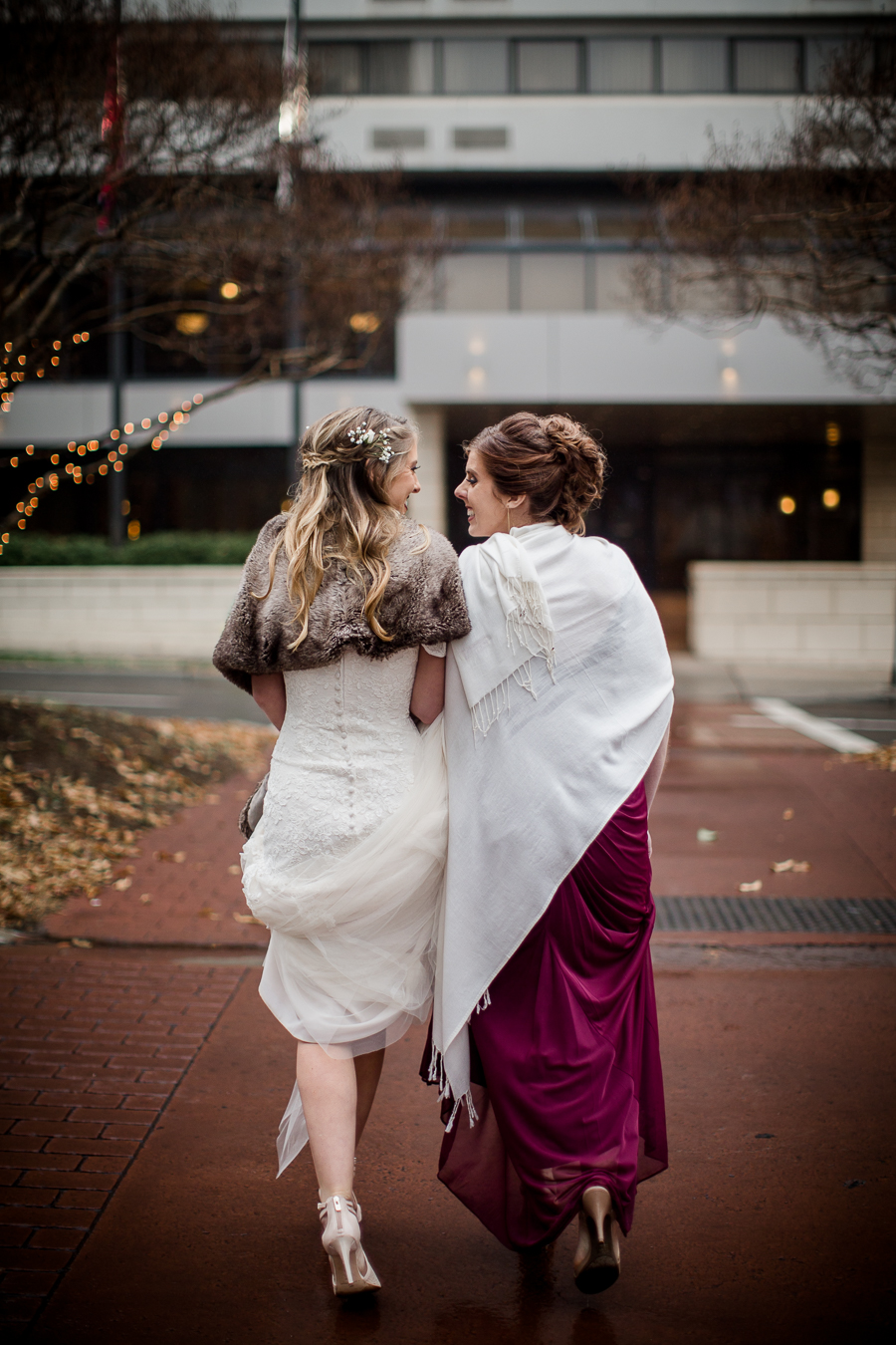Sisters crossing the street arm in arm during the bride and bridesmaids pictures at this winter wedding at Knoxville Wedding Venue, Jackson Terminal, by Knoxville Wedding Photographer, Amanda May Photos.