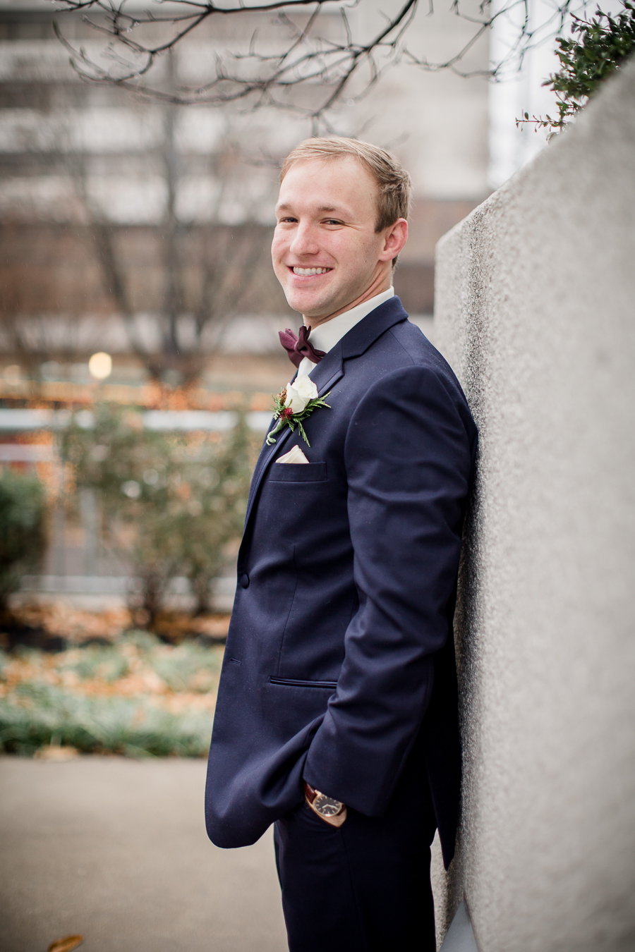 Resting his back against a concrete wall during the groom and groomsmen pictures at this winter wedding at Knoxville Wedding Venue, Jackson Terminal, by Knoxville Wedding Photographer, Amanda May Photos.