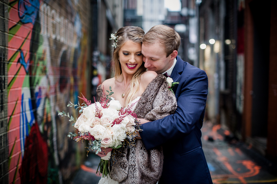 He kisses her shoulder in the art alley during the bride and groom romantic portraits at this winter wedding at Knoxville Wedding Venue, Jackson Terminal, by Knoxville Wedding Photographer, Amanda May Photos.