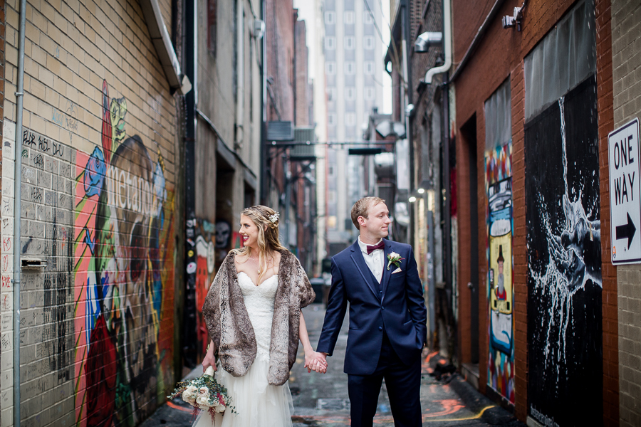 Holding hands looking opposite directions in the art alley during the bride and groom romantic portraits at this winter wedding at Knoxville Wedding Venue, Jackson Terminal, by Knoxville Wedding Photographer, Amanda May Photos.