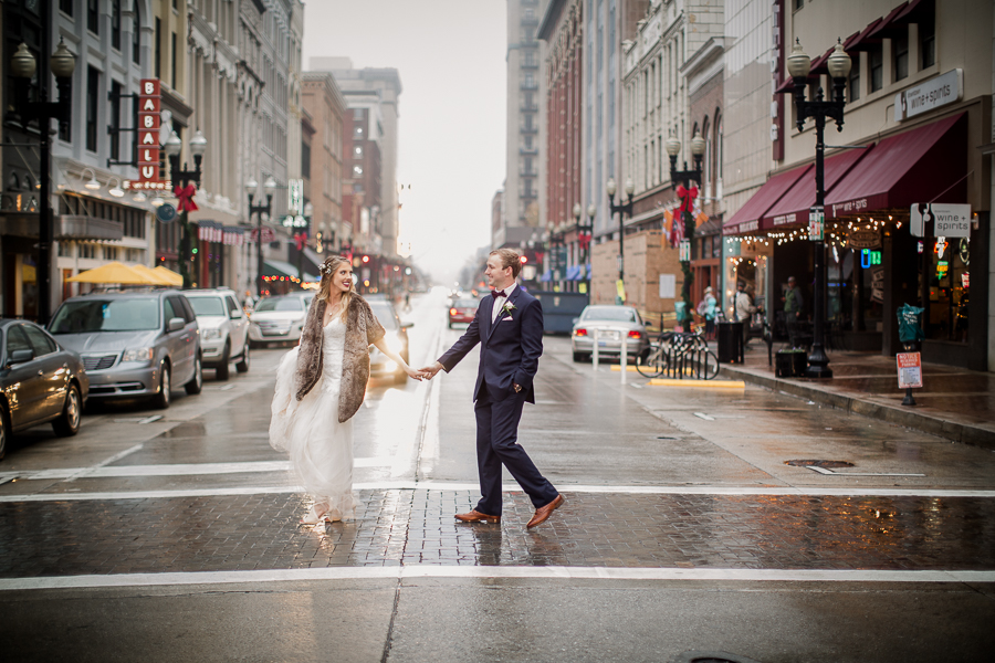Crossing the street hand in hand during the bride and groom romantic portraits at this winter wedding at Knoxville Wedding Venue, Jackson Terminal, by Knoxville Wedding Photographer, Amanda May Photos.