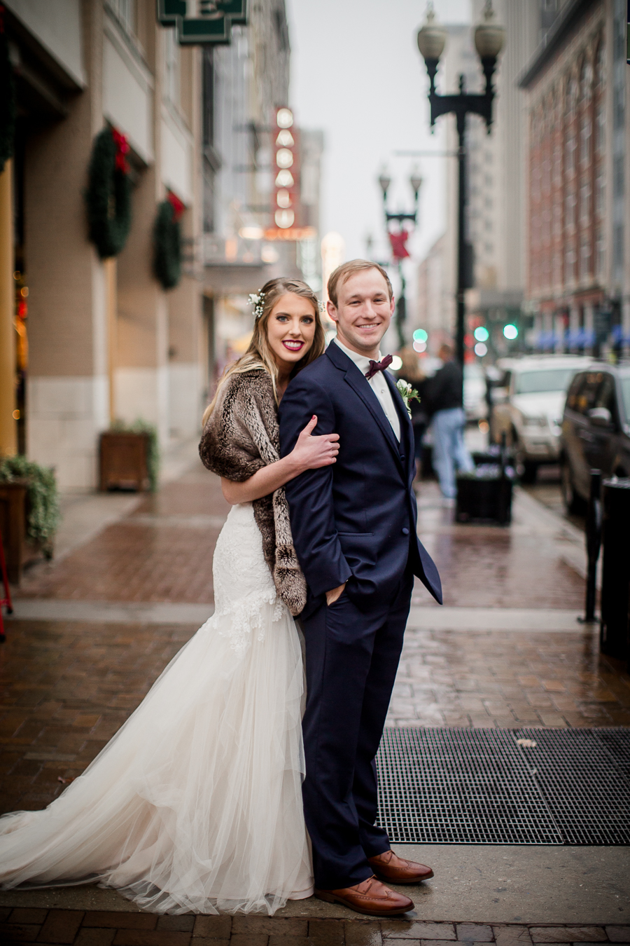 Looking at the camera while the bride hugs the groom from behind during the bride and groom romantic portraits at this winter wedding at Knoxville Wedding Venue, Jackson Terminal, by Knoxville Wedding Photographer, Amanda May Photos.