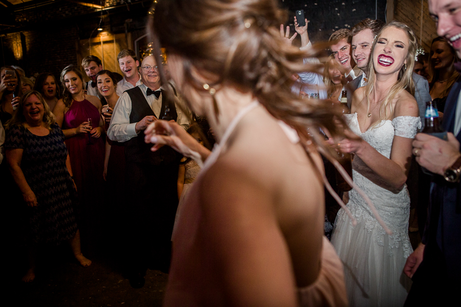 Bride smiling behind her bridesmaid dancing during the dancing reception pictures at this winter wedding at Knoxville Wedding Venue, Jackson Terminal, by Knoxville Wedding Photographer, Amanda May Photos.