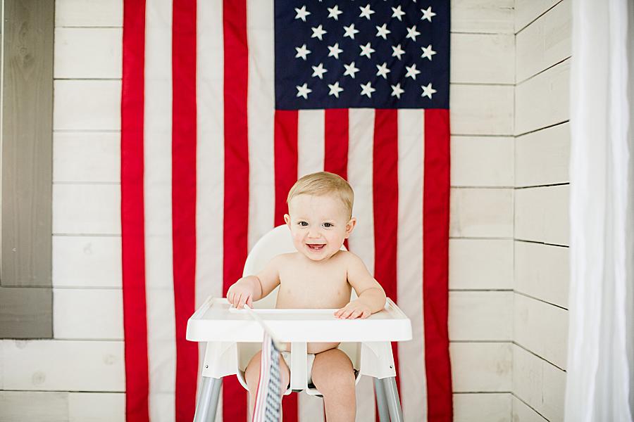american flag behind baby in high chair