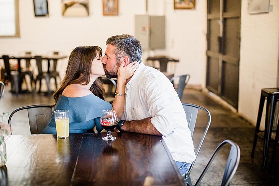 Kissing at a table at this Printshop Brewery engagement by Knoxville Wedding Photographer, Amanda May Photos.