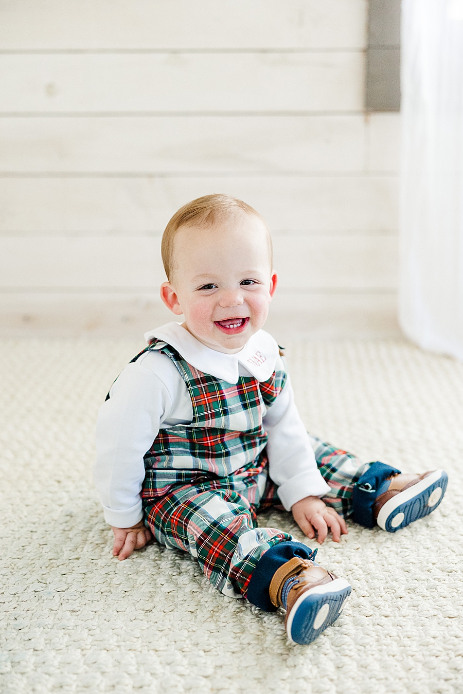 child in Christmas overalls sitting on a jute rug