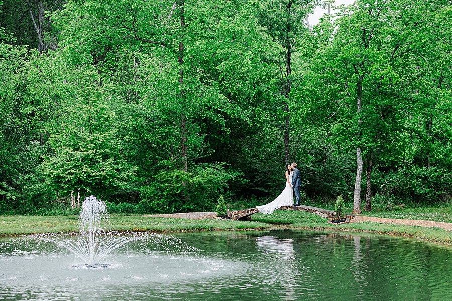 couple on bridge over pond at rainy wedding at ramble creek