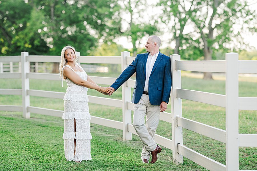 couple holding hands standing by horse pasture