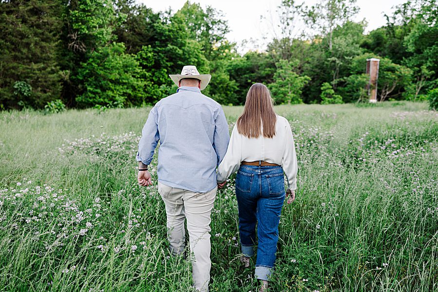 couple holding hands and walking into field of wild flowers