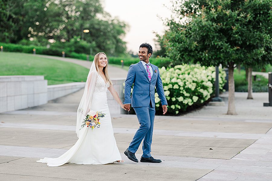 couple in wedding attire walking through park