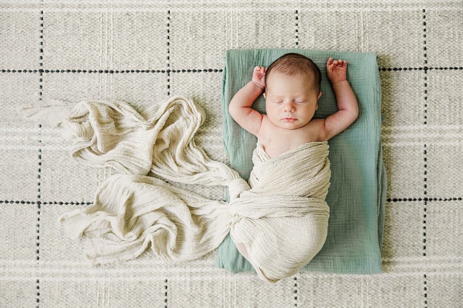 swaddled baby laying on green blanket at home newborn session