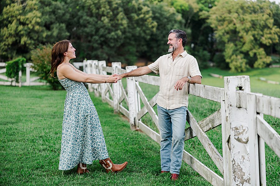 couple standing in front of white fence at horse farm engagement