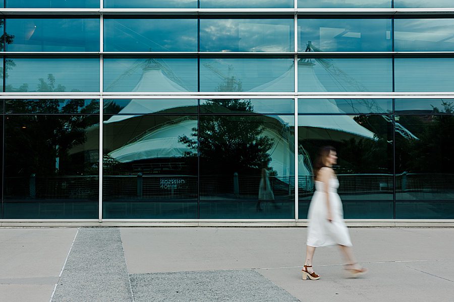 woman in white sundress walking in front of reflective windows at colorful stairs senior session
