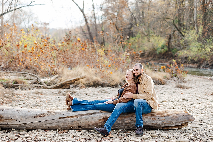 couple sitting on driftwood by little river