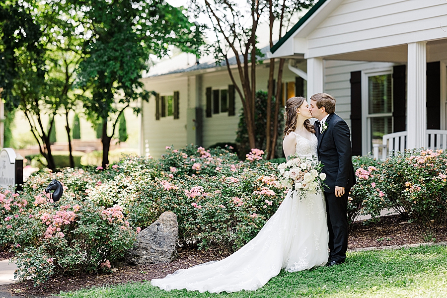 Kissing in front of the flowers at Julianna Wedding by Amanda May Photos