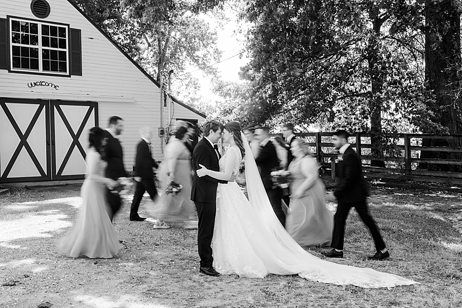 Bride and groom hug with wedding party in the background at wedding by Amanda May Photos