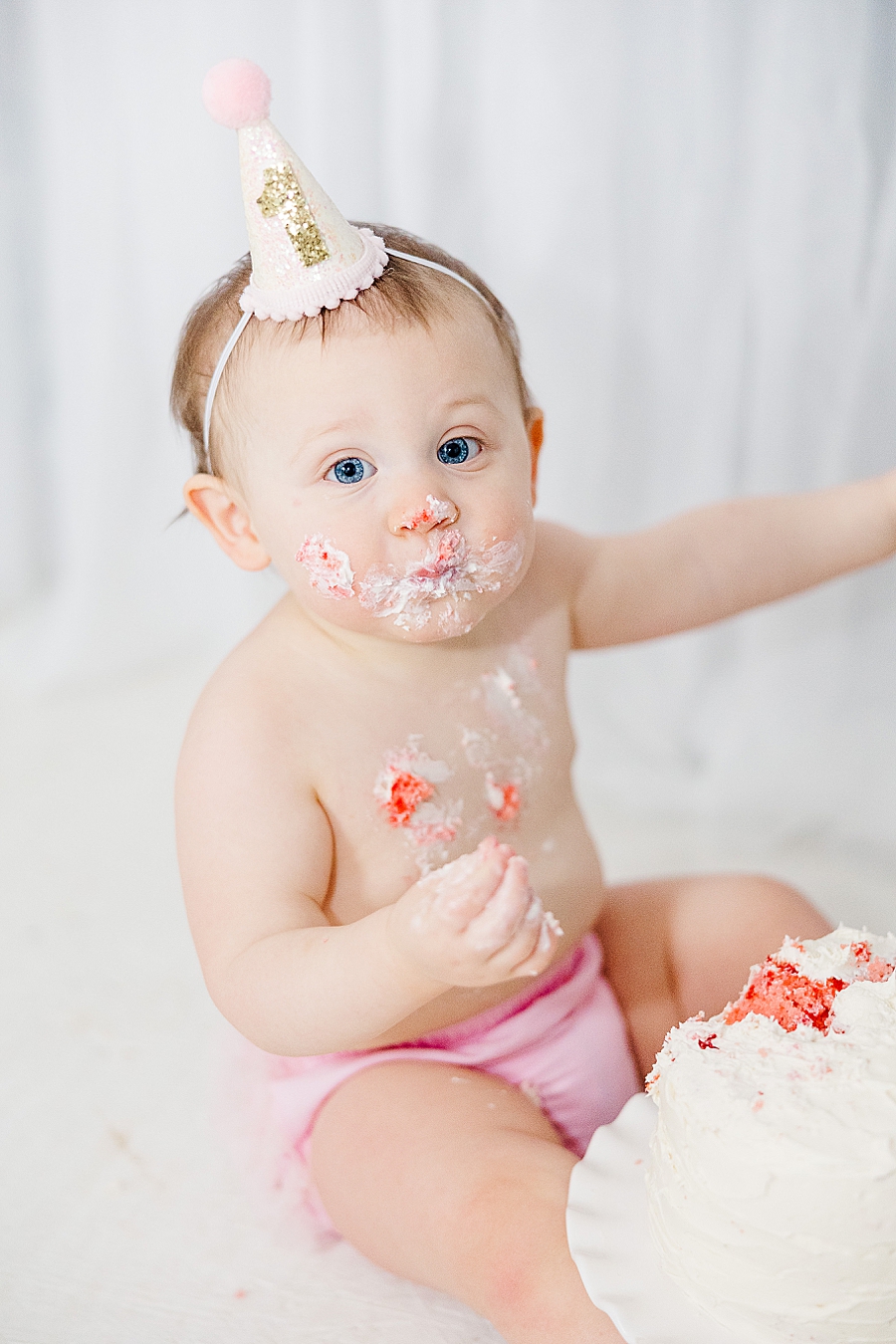 Baby girl covered in icing at cake smash