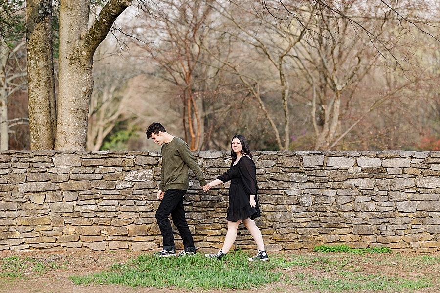 couple walking by stone wall during knoxville botanical engagement