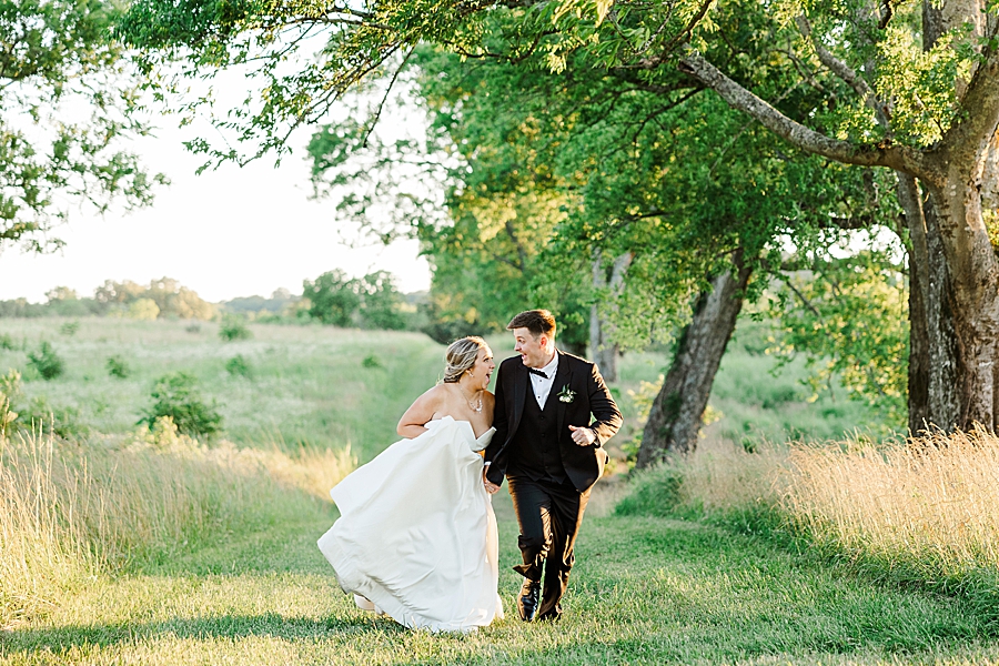 bride and groom running through marblegate field