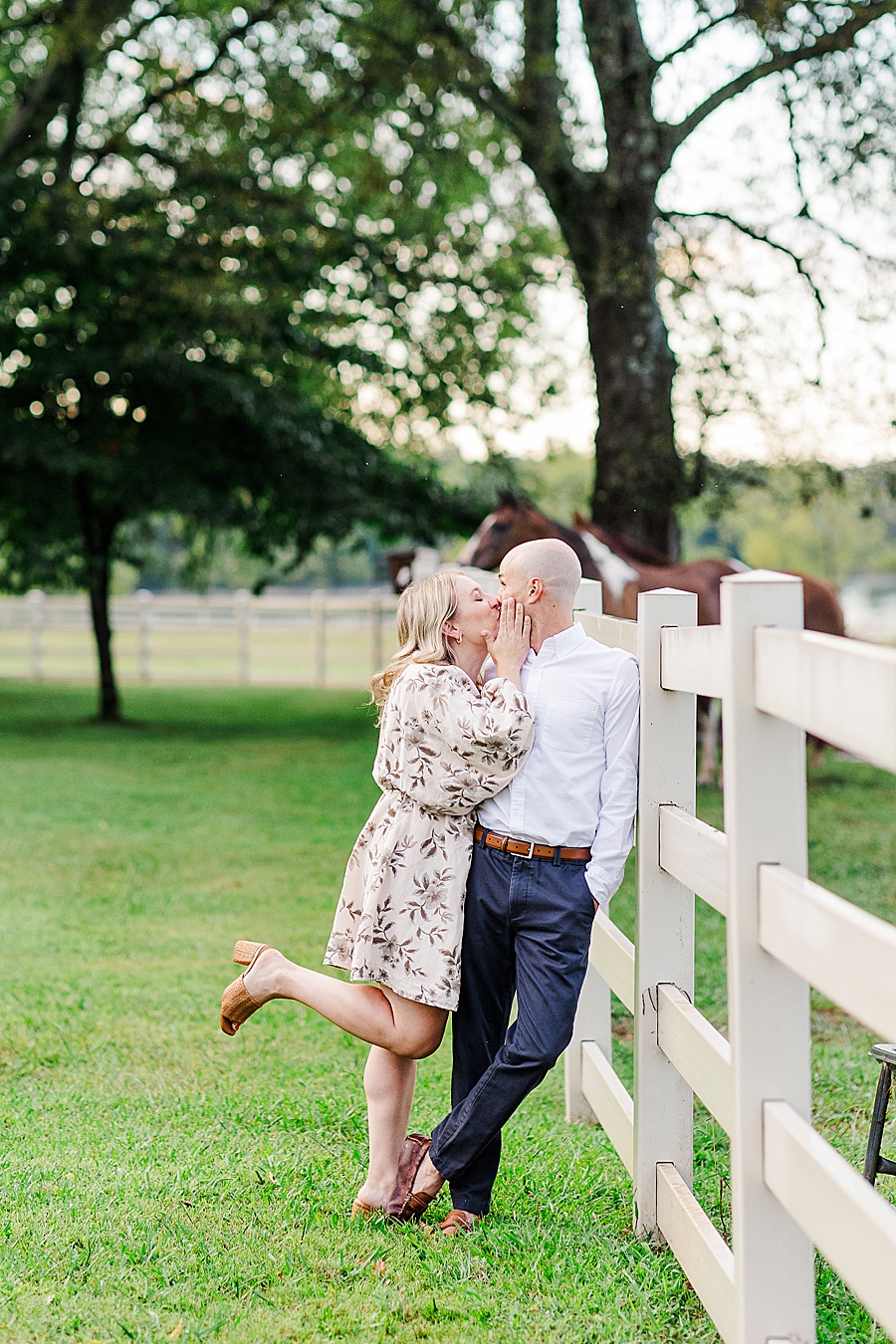 couple leaning against white horse fence