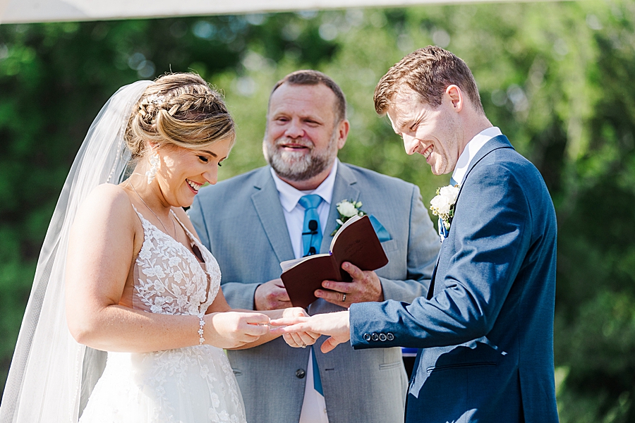 Bride placing ring on groom's finger at wedding by Amanda May Photos