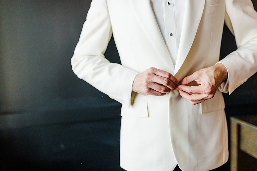 groom buttoning white tuxedo jacket