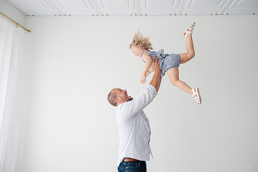 dad tossing daughter at white room baby boy