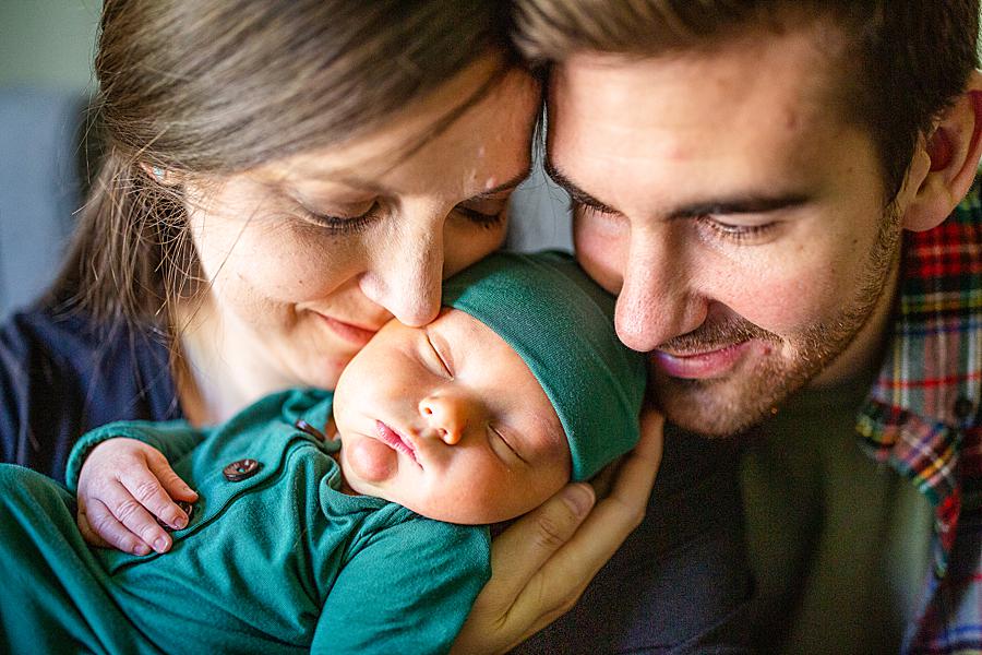Mom and dad snuggling newborn in green hat at knoxville newborn session